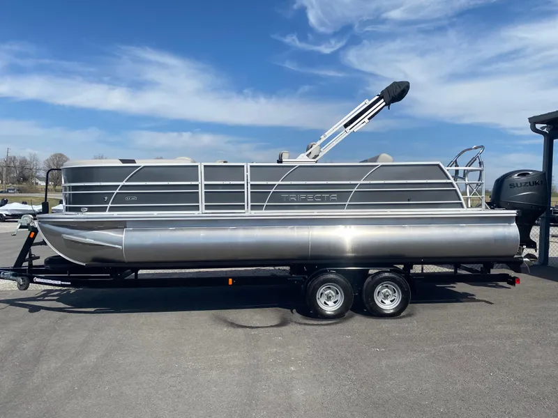 Slide: The Image of 2025 Trifecta LE Series 22UL pontoon boat on trailer, parked outdoors under blue sky. - 3
