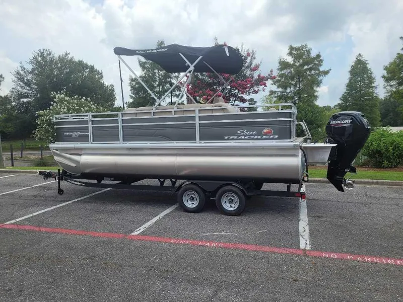 The Image of 2025 Sun Tracker Fishin' Barge 20 DLX pontoon boat on trailer in parking lot. - 0