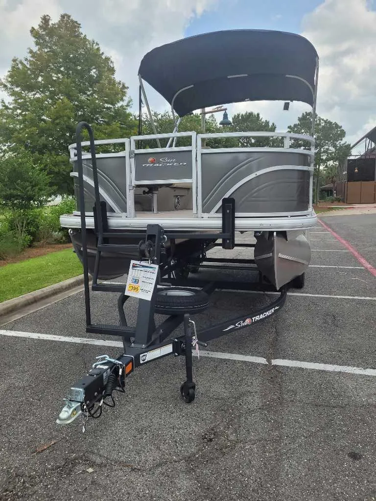 Slide: The Image of 2025 Sun Tracker Fishin' Barge 20 DLX pontoon boat on trailer in parking lot. - 2