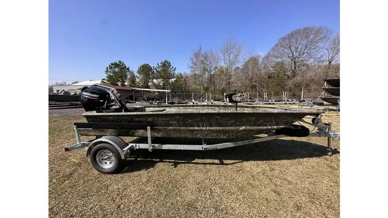 Slide: The Image of 2025 War Eagle 750 Gladiator boat on trailer, parked on grass, with trees in background. - 1