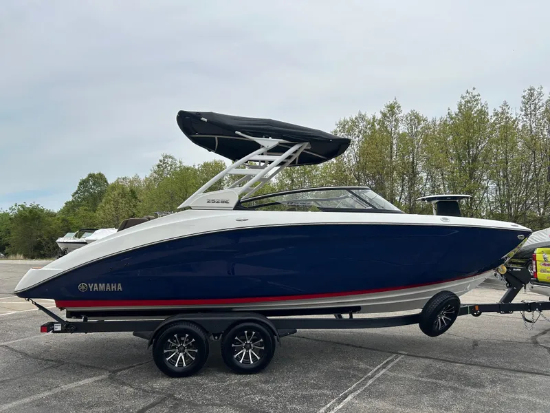 Slide: The Image of 2025 Yamaha Boats 252SE on trailer, sleek design, blue hull, black canopy, parked outdoors. - 4