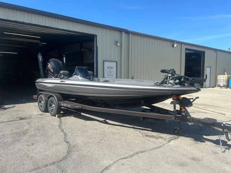 Slide: The Image of 2025 Skeeter ZXR20 boat on trailer outside a garage under clear blue sky. - 1