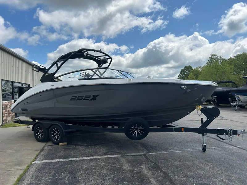 Slide: The Image of 2025 Yamaha Boats 252XE on trailer, parked outdoors under a partly cloudy sky. - 1