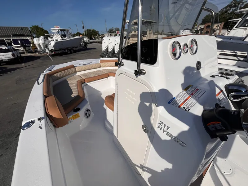 Slide: The Image of 2025 NauticStar 211 Hybrid boat with tan seating and modern dashboard in a marina setting. - 10