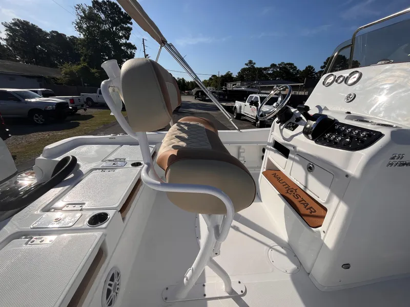 Slide: The Image of 2025 NauticStar 211 Hybrid boat interior with helm and seating, under clear blue sky. - 4