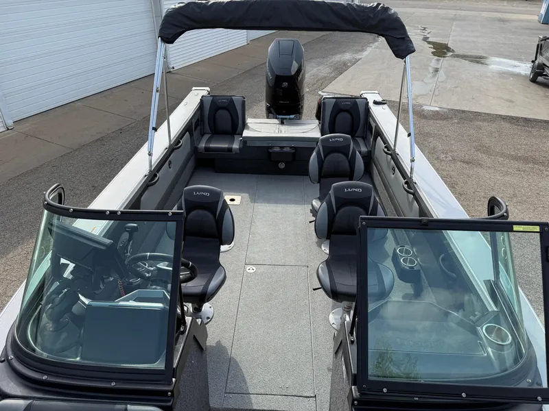 Slide: The Image of 2023 Lund 2275 Baron boat interior with seating and windshield, docked on pavement. - 12