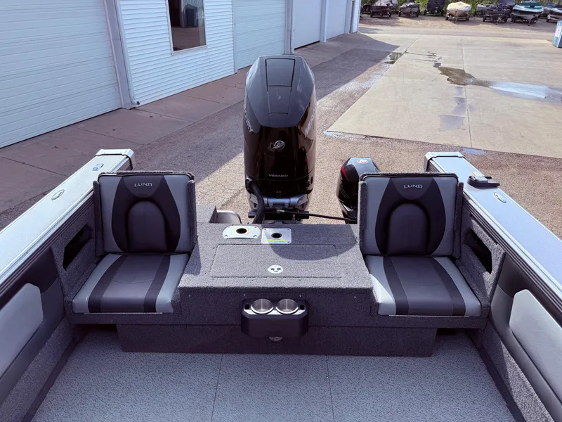 Slide: The Image of 2023 Lund 2275 Baron boat interior with seating and motor, parked near a building. - 25