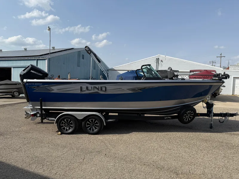 Slide: The Image of 2023 Lund 2275 Baron boat on trailer, parked outdoors under a clear sky. - 3