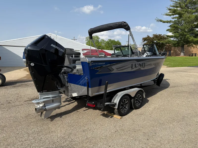 Slide: The Image of 2023 Lund 2275 Baron boat on trailer, blue and silver, with Mercury outboard motor. - 4