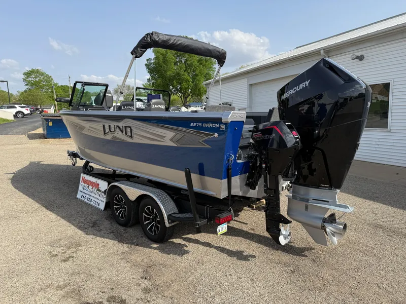 Slide: The Image of 2023 Lund 2275 Baron boat with Mercury engine on trailer, parked outdoors. - 6