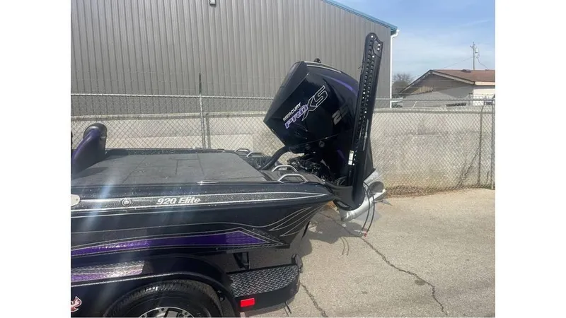 Slide: The Image of 2025 Phoenix 920 Elite boat with powerful outboard motor, parked near a fence. - 2