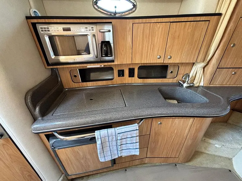 Slide: The Image of 2006 Sea Ray 320 Sundancer kitchen with microwave, sink, and wooden cabinets. - 16