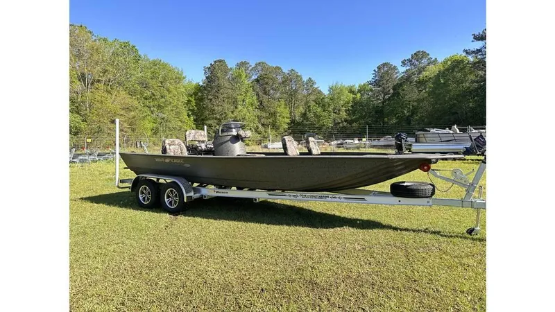 Slide: The Image of 2025 War Eagle 2170 Blackhawk boat on trailer, parked on grass with trees in background. - 1