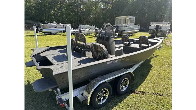 Slide: The Image of 2025 War Eagle 2170 Blackhawk boat on trailer, parked on grass, with other boats in background. - 2
