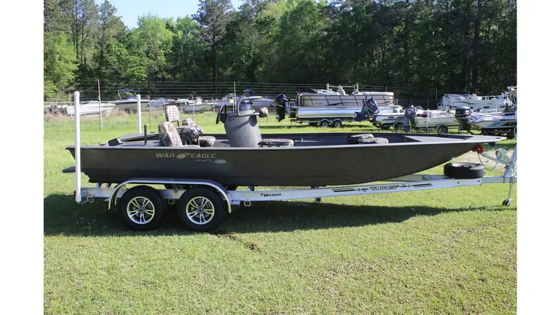 Slide: The Image of 2025 War Eagle 2170 Blackhawk boat on trailer in grassy area with trees. - 9