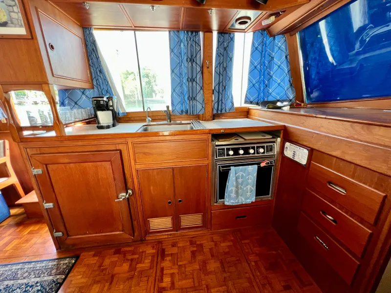 Slide: The Image of 1985 Grand Banks 42 Motoryacht kitchen with wood cabinetry, stove, and blue curtains. - 23