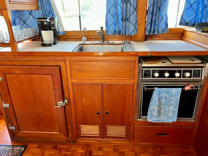 Slide: The Image of 1985 Grand Banks 42 Motoryacht kitchen with wooden cabinetry, sink, oven, and blue curtains. - 25