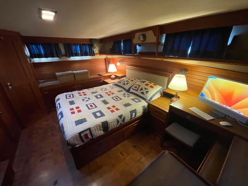 Slide: The Image of 1985 Grand Banks 42 Motoryacht bedroom with cozy bed, wooden interior, and computer setup. - 33