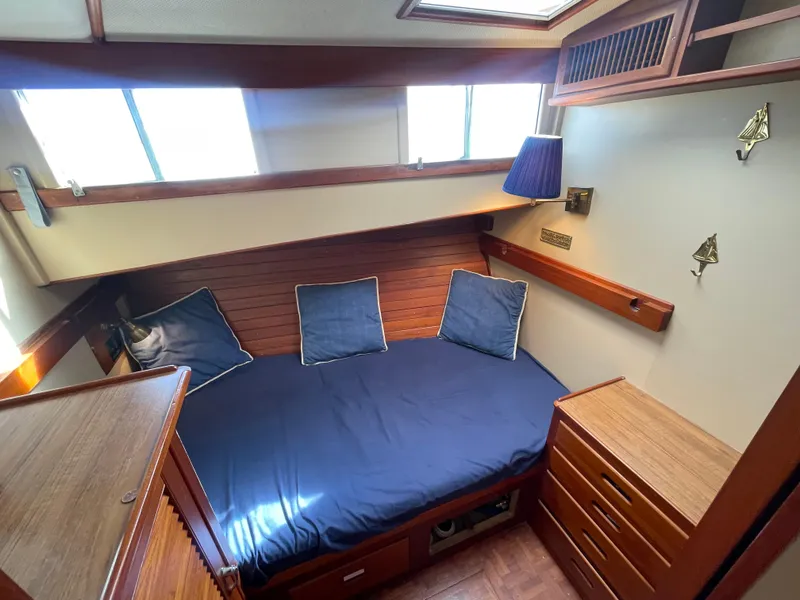 Slide: The Image of 1985 Grand Banks 42 Motoryacht cabin with blue bedding, wooden furnishings, and natural light. - 48