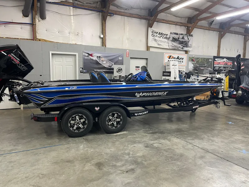 Slide: The Image of 2025 Phoenix 21 XE boat in showroom, blue and black design, on trailer. - 2