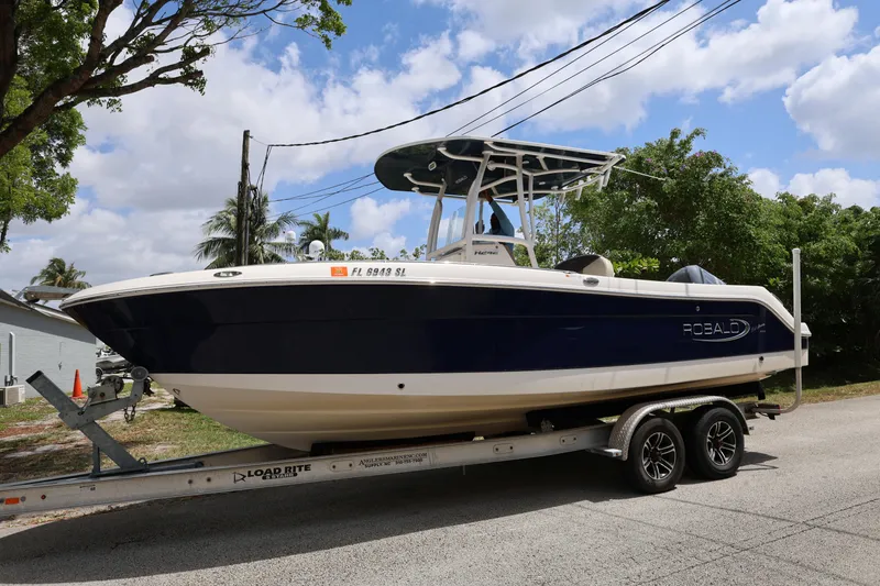 Slide: The Image of 2019 Robalo R242 Explorer boat on trailer, parked roadside under blue sky. - 1