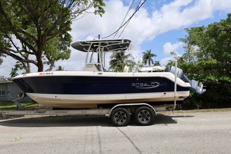 Slide: The Image of 2019 Robalo R242 Explorer boat on trailer, parked on a sunny street. - 2