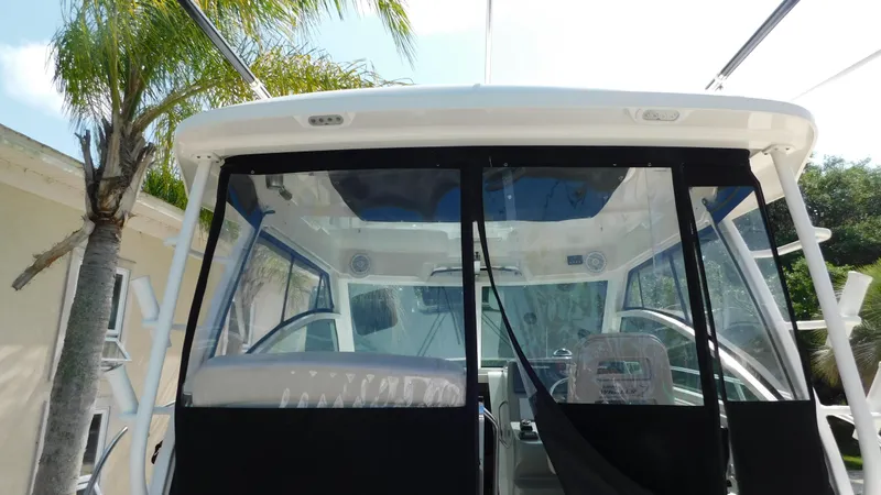 Slide: The Image of 2017 Boston Whaler 315 Conquest boat cockpit with clear enclosure and palm tree in background. - 37