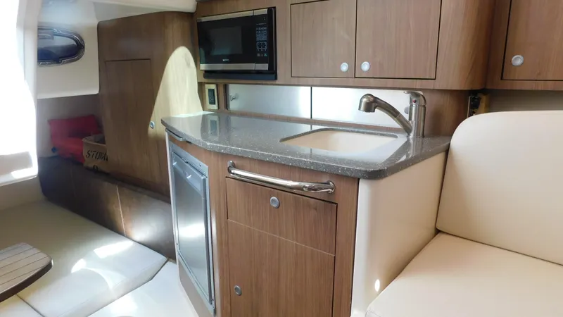 Slide: The Image of 2017 Boston Whaler 315 Conquest interior with kitchenette, featuring wood cabinets and modern appliances. - 7