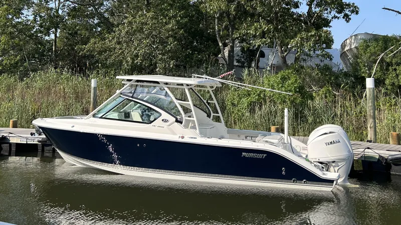 Slide: The Image of 2026 Pursuit DC 266 Dual Console boat docked by lush greenery. - 0