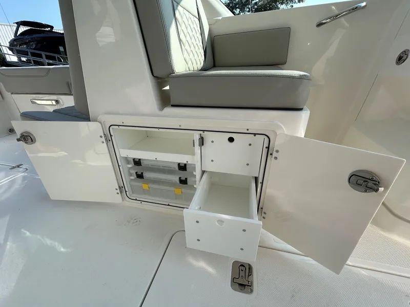 Slide: The Image of 2026 Pursuit DC 266 Dual Console boat storage compartment with open doors and drawers. - 11