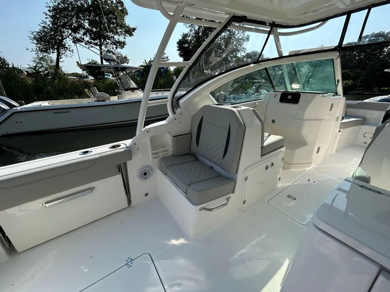 Slide: The Image of 2026 Pursuit DC 266 Dual Console boat interior with seating and helm, docked near trees. - 9