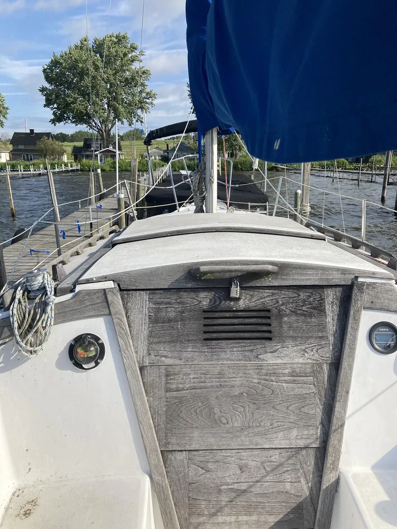 Slide: The Image of 1980 Catalina Cat 27 sailboat docked, featuring wooden deck and blue sail cover. - 5