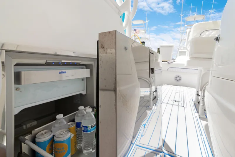 Slide: The Image of 2004 Intrepid 377 Walkaround boat interior with open fridge, stocked with drinks, under a clear sky. - 6