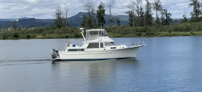 Slide: The Image of 1981 Tollycraft 43 Motoryacht cruising on a serene lake with forested hills in the background. - 0