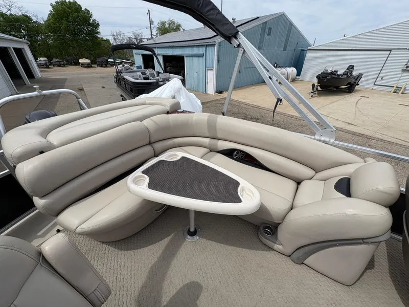 Slide: The Image of 2011 Sun Tracker PARTY BARGE 25 with beige seating and a small table, docked near blue buildings. - 22