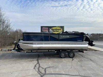 Slide: The Image of 2025 Lowe LS 210 WT pontoon boat on trailer, parked near Blackbeard Marine sign. - 0