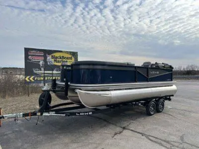 Slide: The Image of 2025 Lowe LS 210 WT pontoon boat on trailer, parked near BlackBeard Marine sign. - 7