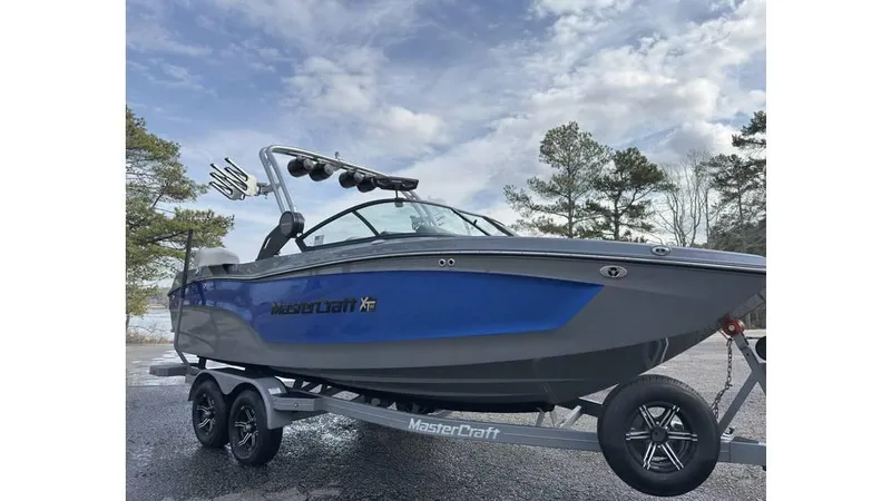 Slide: The Image of 2023 MasterCraft XT22 boat on trailer, blue and gray design, parked outdoors. - 2