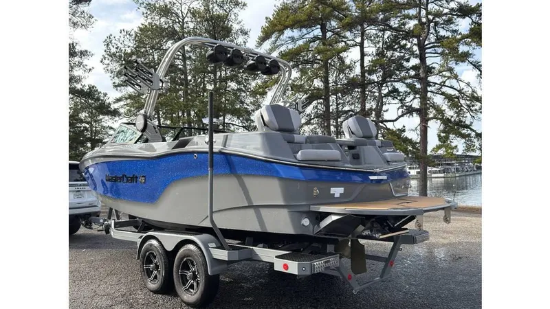 Slide: The Image of 2023 MasterCraft XT22 boat on trailer, parked near trees and water. - 3