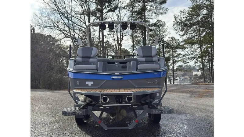 Slide: The Image of 2023 MasterCraft XT22 boat, rear view, parked on a wet surface with trees in the background. - 4