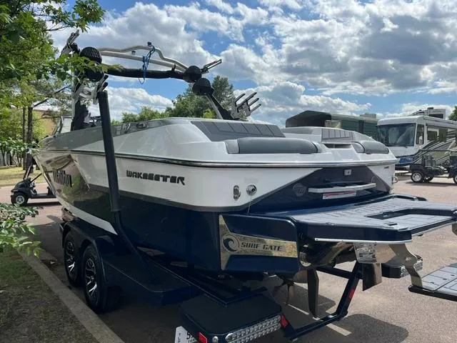 Slide: The Image of 2023 Malibu Wakesetter 24 MXZ boat on trailer, parked outdoors under a partly cloudy sky. - 3