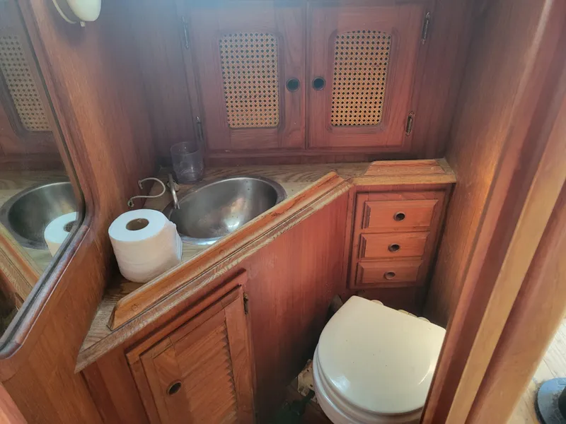 Slide: The Image of 1977 Islander 27 boat bathroom with wooden cabinets, sink, and toilet. - 17