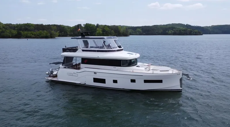 Slide: The Image of 2021 Sirena 58 yacht cruising on a serene lake with lush green shoreline. - 13