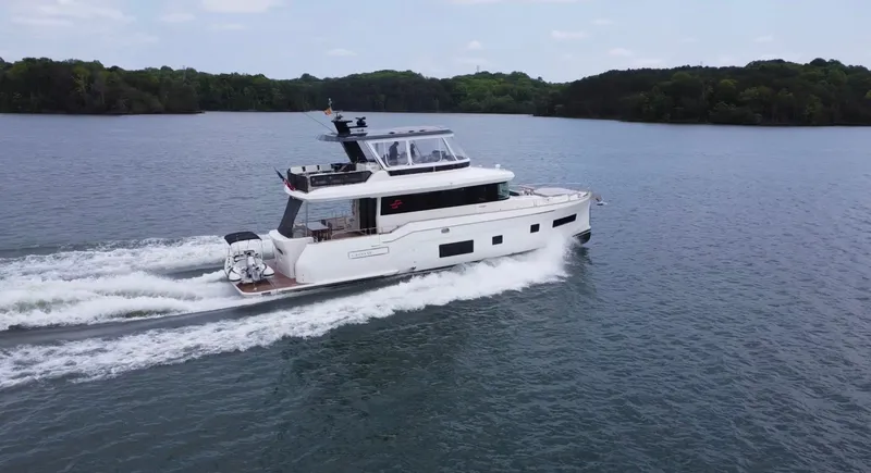 Slide: The Image of 2021 Sirena 58 yacht cruising on a serene lake with lush green shoreline. - 7