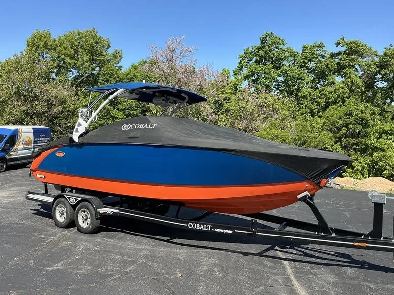 Slide: The Image of 2021 Cobalt R7 Surf boat on trailer, blue and orange design, parked outdoors. - 1