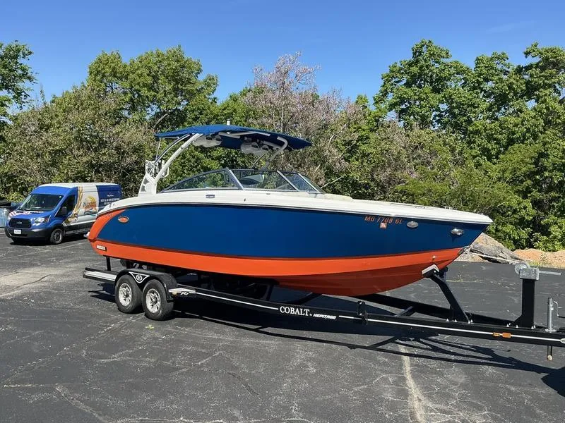 Slide: The Image of 2021 Cobalt R7 Surf boat on trailer, blue and orange design, parked outdoors. - 2
