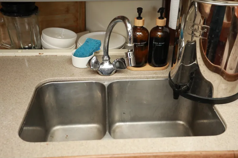 Slide: The Image of Stainless steel double sink with faucet, soap dispensers, and sponge on countertop. - 24