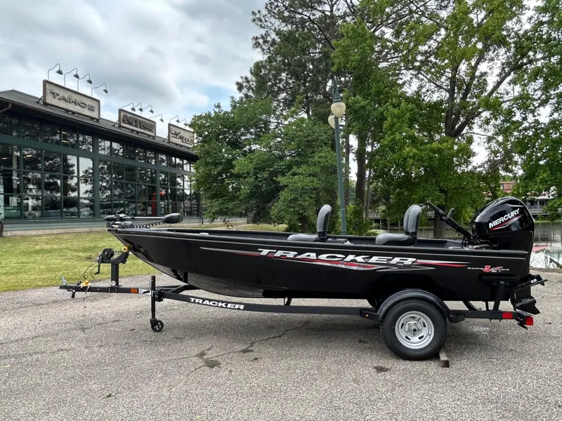 Slide: The Image of 2025 Tracker Super Guide V-16 T boat on trailer, parked outdoors near trees and building. - 28