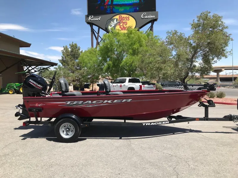 Slide: The Image of 2025 Tracker Super Guide V-16 T boat on trailer, parked outdoors near trees and a sign. - 2