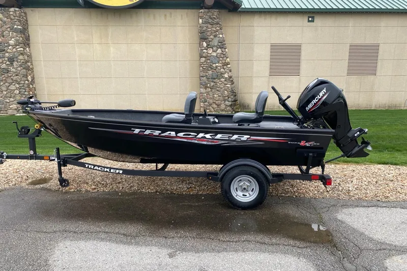 The Image of 2025 Tracker Super Guide V-16 T fishing boat on trailer, parked outdoors. - 0
